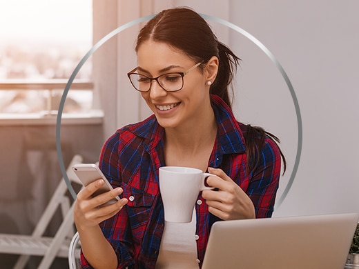 Woman wearing glasses, laughing and looking at cell phone, holding a cup of coffee in hand